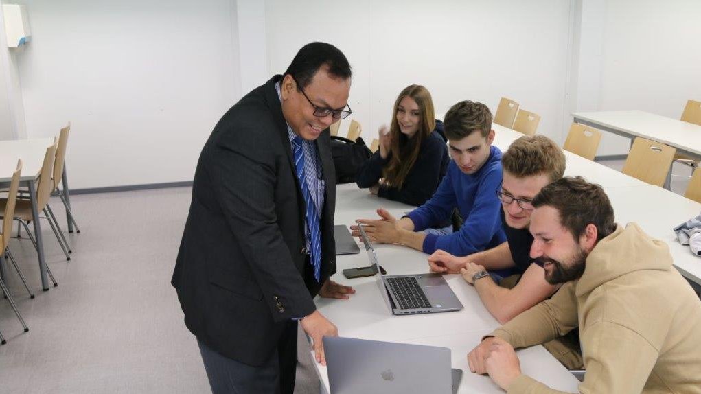 Ein Dozent erklärt Studierenden etwas am Laptop