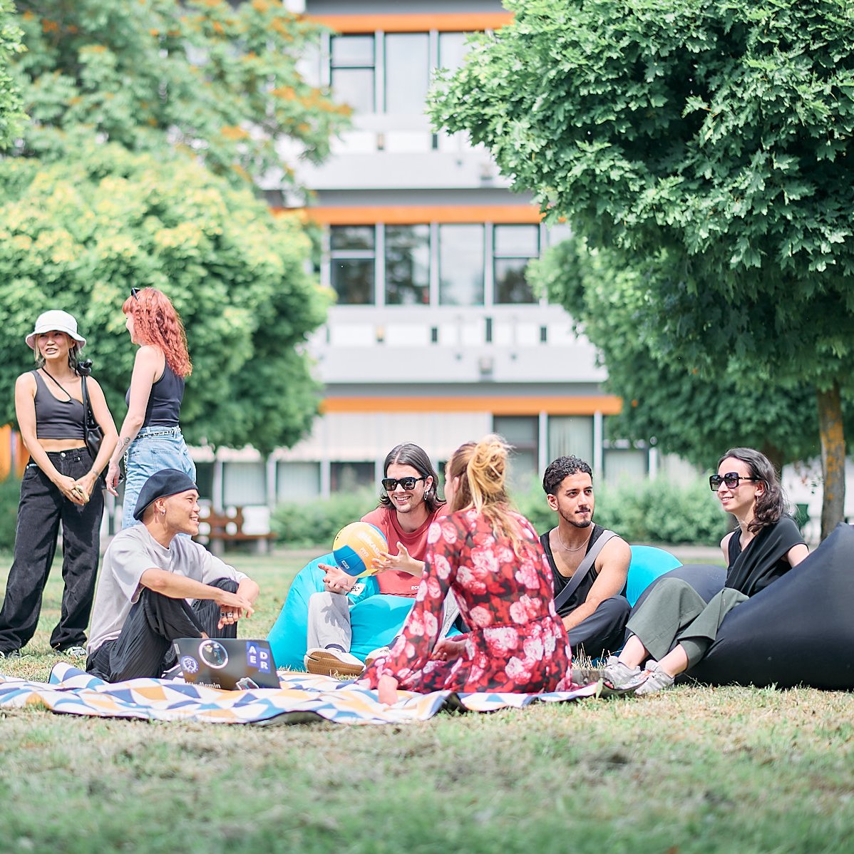 Studierende sitzen entspannt auf Decken im Gras und unterhalten sich