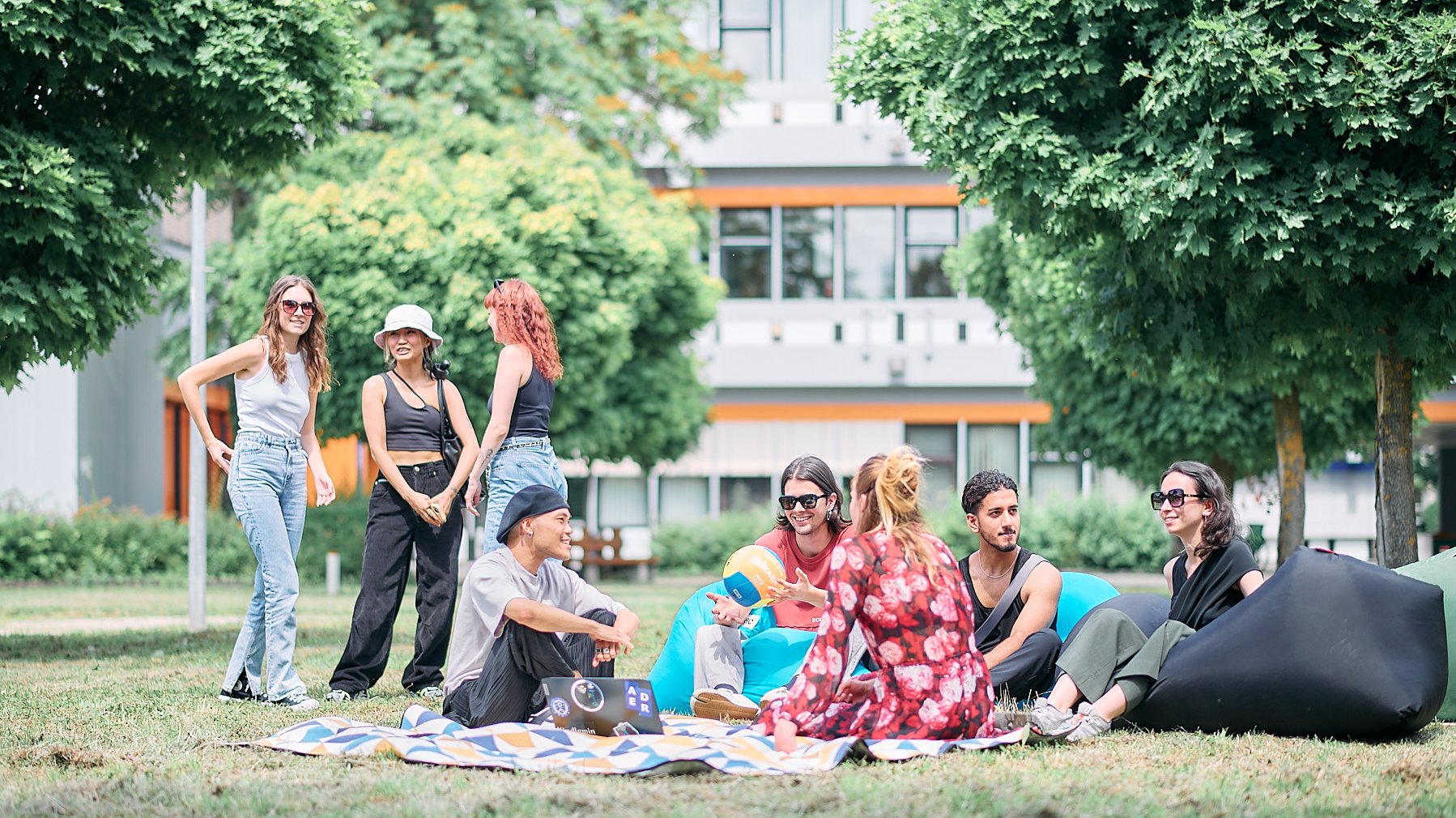 Studierende sitzen entspannt auf Decken im Gras und unterhalten sich