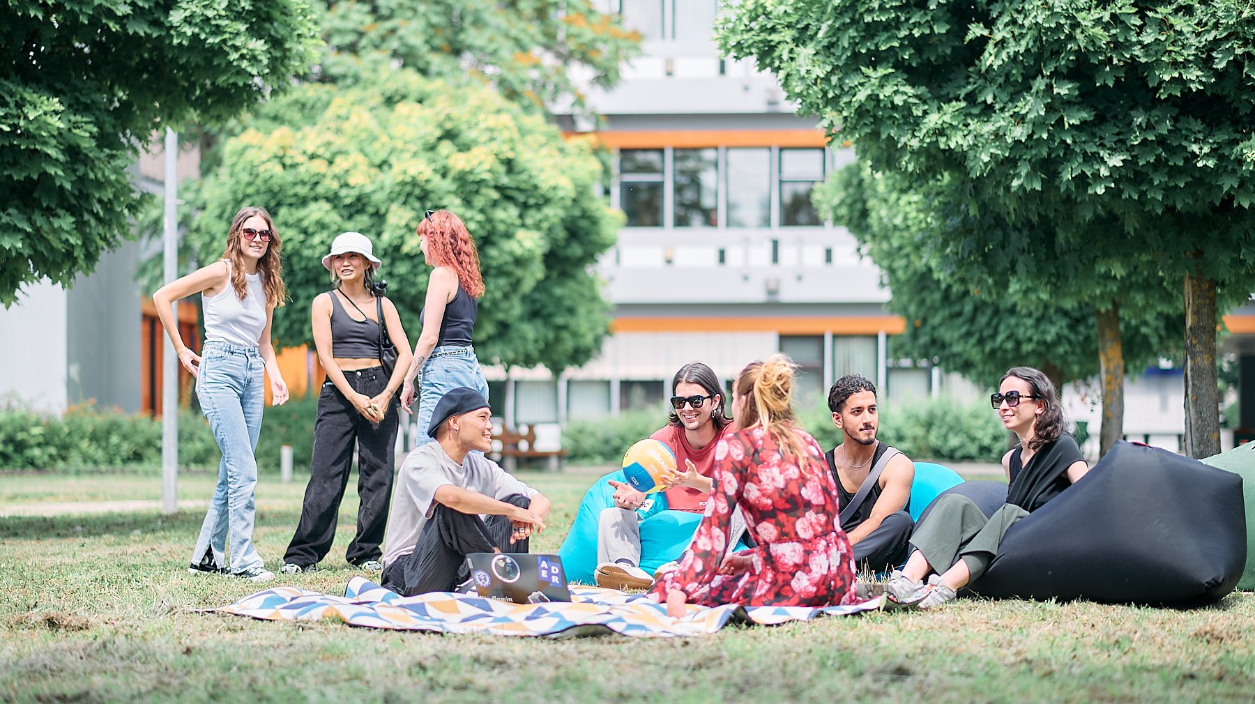 Studierende sitzen entspannt auf Decken im Gras und unterhalten sich