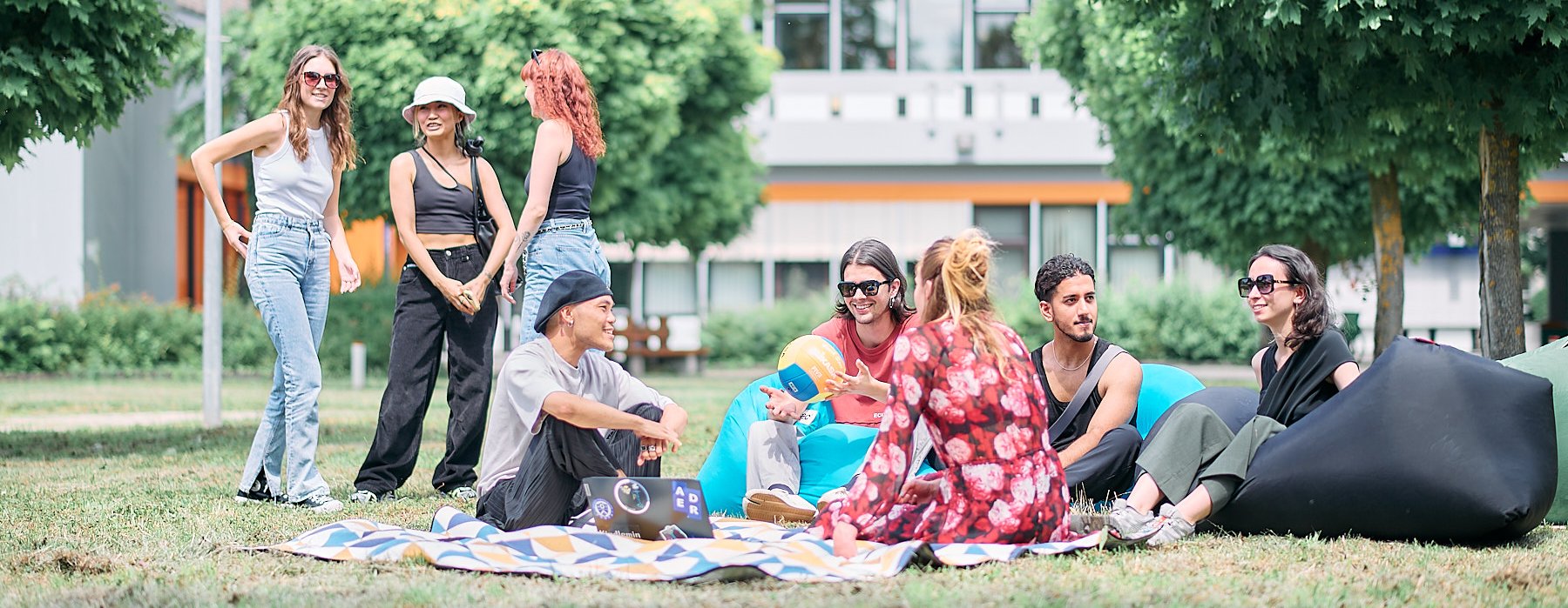 Studierende sitzen entspannt auf Decken im Gras und unterhalten sich