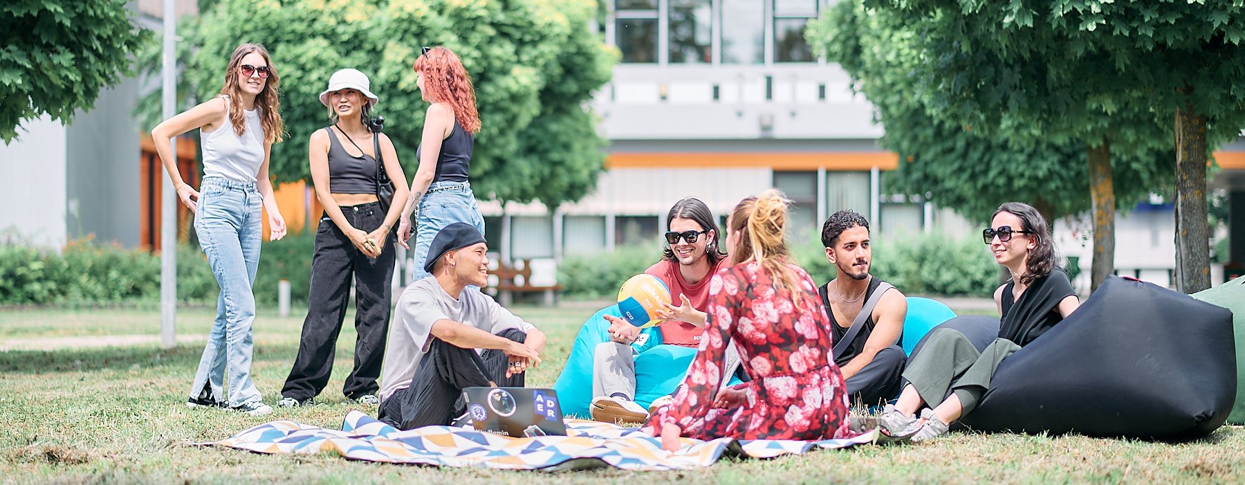 Studierende sitzen entspannt auf Decken im Gras und unterhalten sich