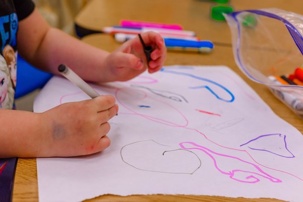 Kleinkind malt mit bunten Wachsstiften auf ein Blatt Papier