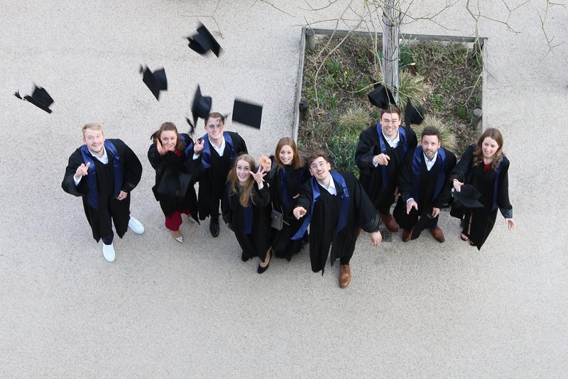 Absolventinnen und Absolventen in Roben werfen fröhlich ihre Hüte in die Luft