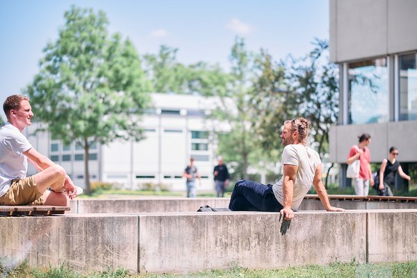 Zwei Studierende genießen die Sonne in der Mittagspause am Freilufthörsaal