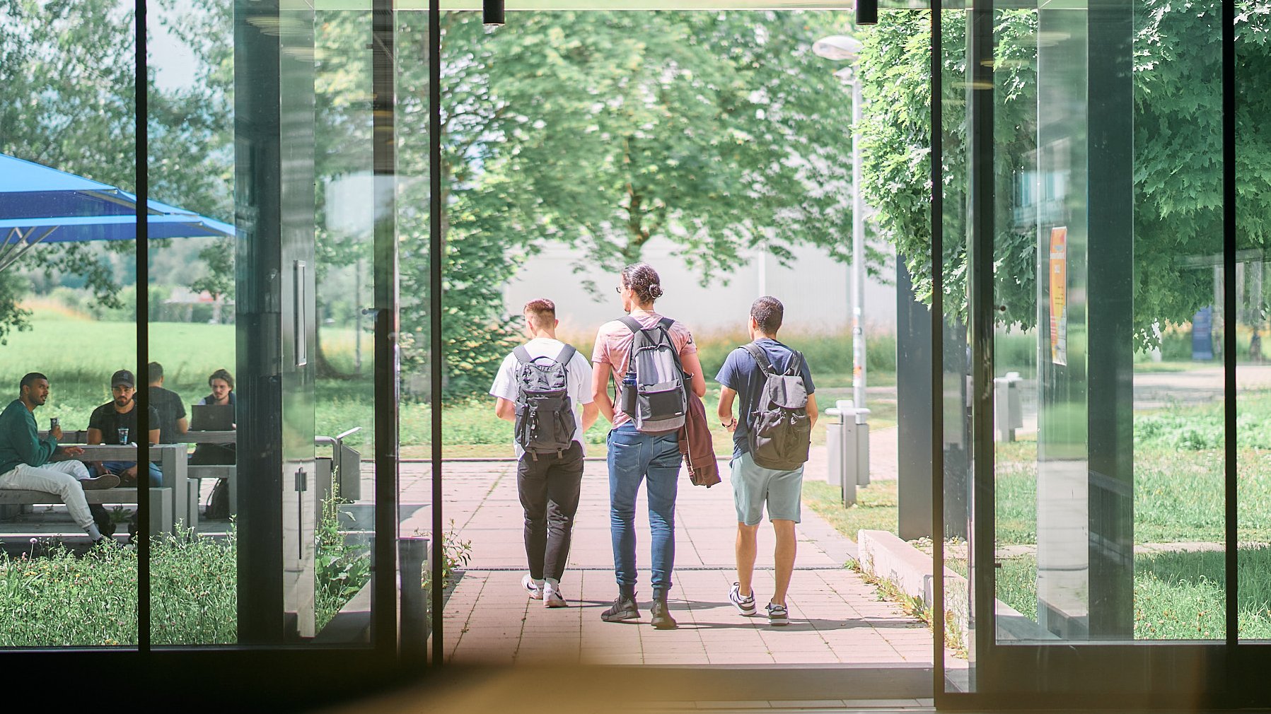 Studierende laufen aus einem Gebäude raus in die Sonne