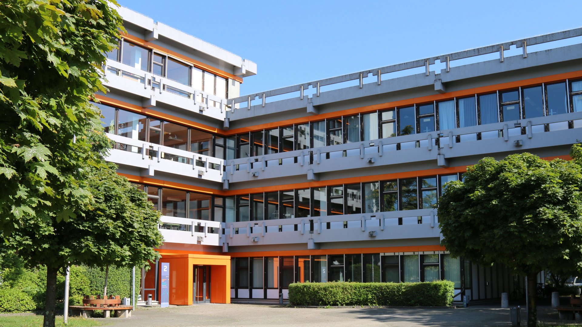 Dreistöckiges Gebäude mit orangener Fassade und Grünfläche im Sommer