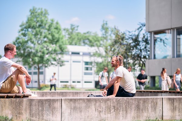 Zwei Studierende sitzen bei sonnigem Wetter im Freilufthörsaal und unterhalten sich