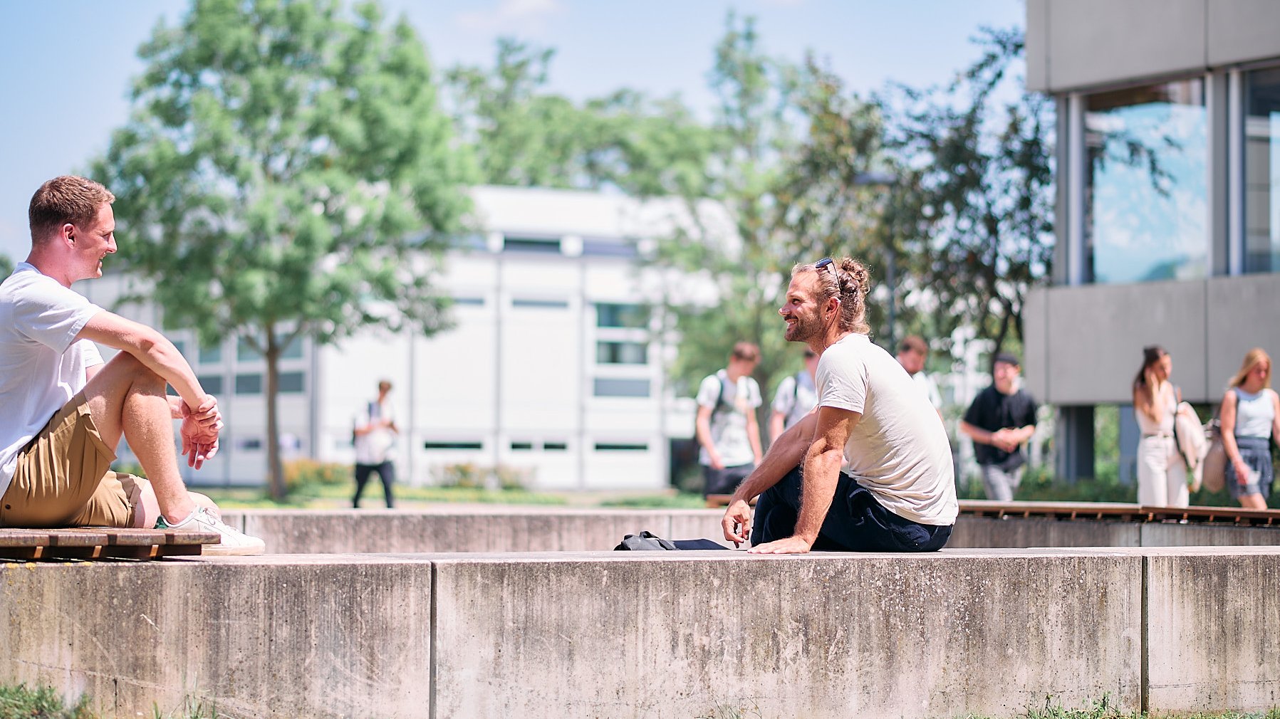 Zwei Studierende sitzen bei sonnigem Wetter im Freilufthörsaal und unterhalten sich